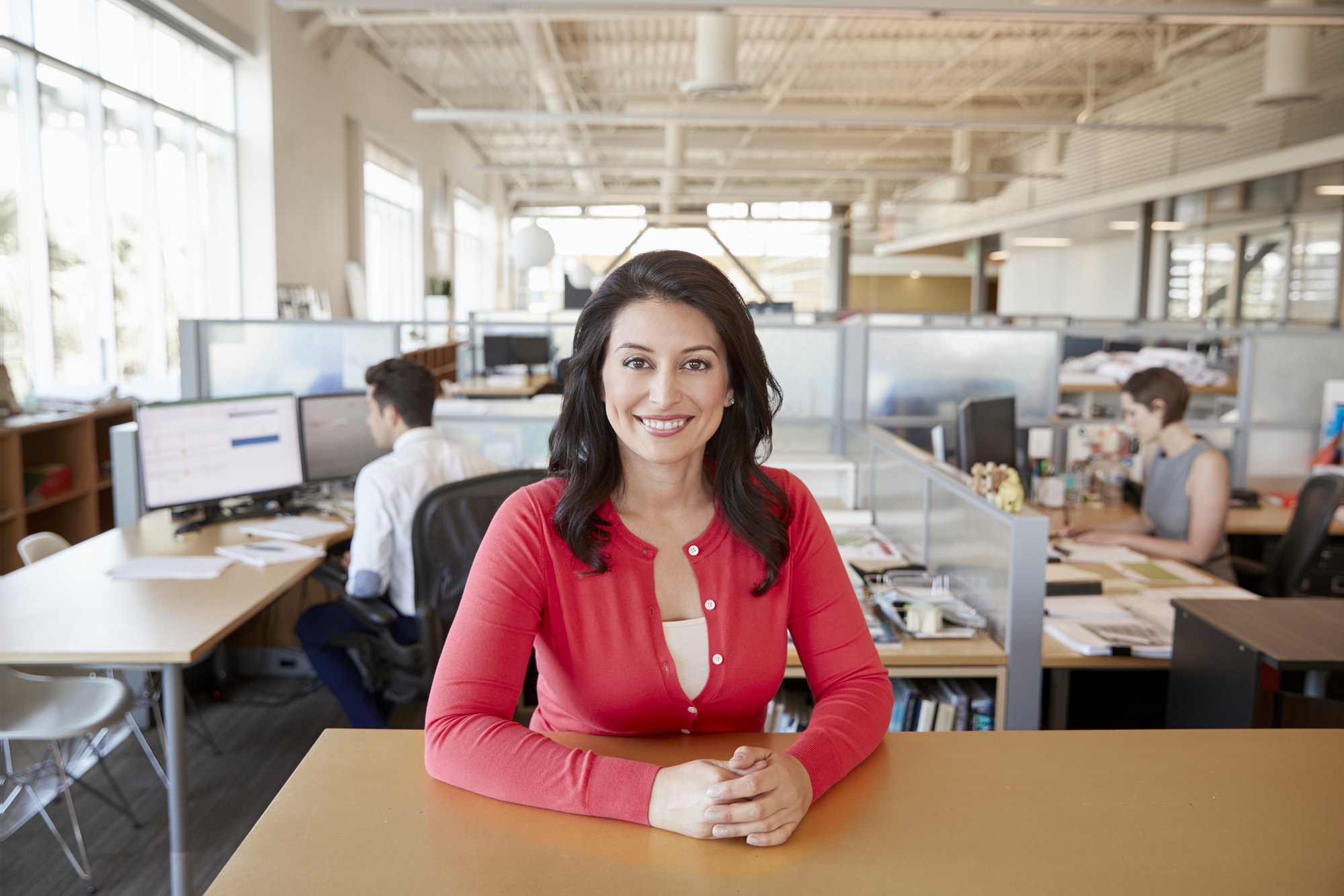Smiling female architect at a desk in busy open plan office